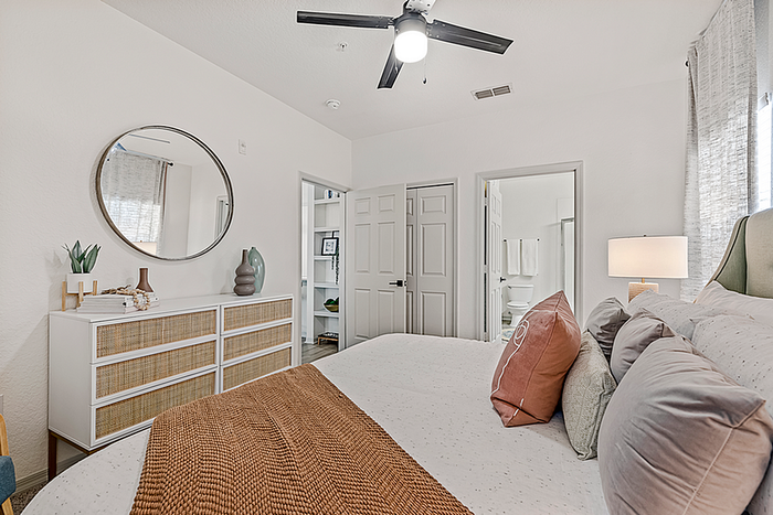 Inviting bedroom with elegant decor, featuring a plush bed, stylish dresser, and modern ceiling fan, leading to en-suite bathroom.