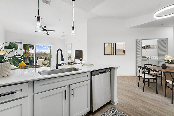 Modern open-concept kitchen and living room with stylish white cabinetry, sleek appliances, and a view of a scenic balcony from the dining area.