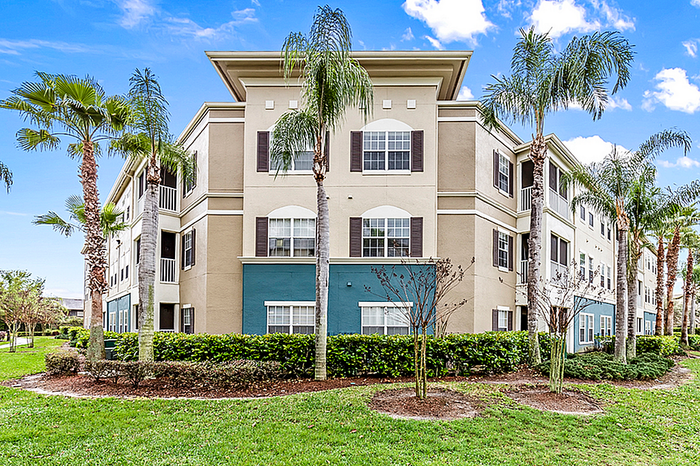 Charming apartment building surrounded by lush palm trees and greenery under a clear blue sky.