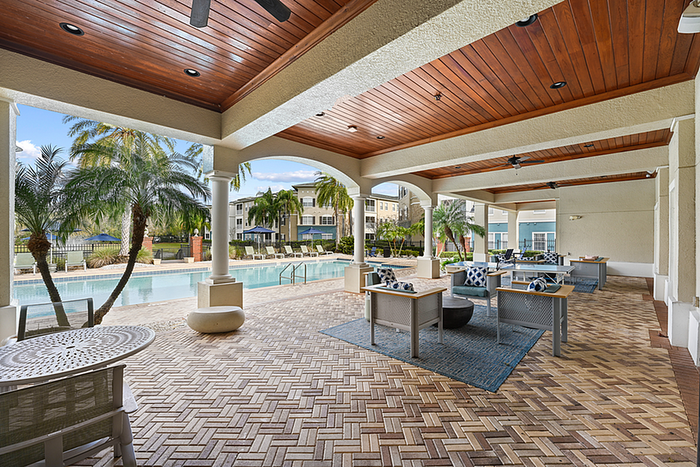 Luxurious outdoor lounge with elegant wood ceilings overlooking a pristine swimming pool and lush palm trees.