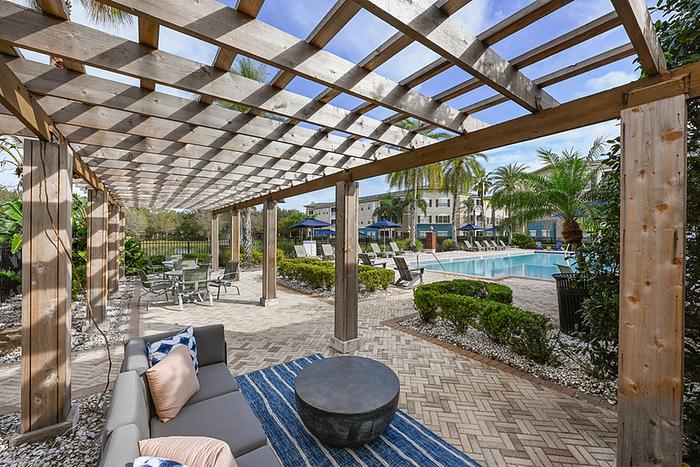 Chic outdoor lounge space with shaded pergola and inviting poolside area, surrounded by lush palm trees and comfortable seating.