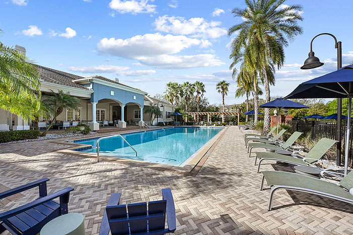 Luxurious outdoor swimming pool area with tropical landscaping, sun loungers, and a modern clubhouse, perfect for relaxation and leisure.