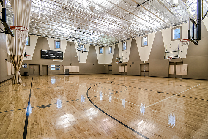 Spacious indoor basketball court with polished wood flooring, bright lighting, and multiple hoops, perfect for sports enthusiasts.
