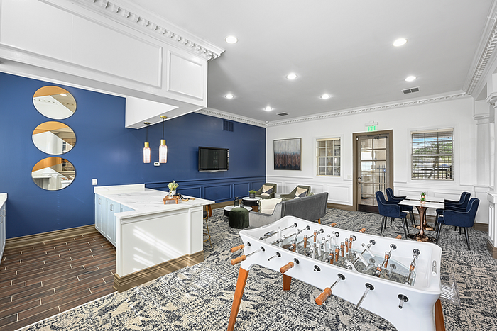 Modern and inviting clubhouse space with elegant blue accent wall, chic seating area, and a stylish foosball table, perfect for socializing and relaxation.