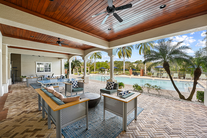 Outdoor lounge with comfortable seating overlooking a sparkling pool and lush palm trees in a serene setting.