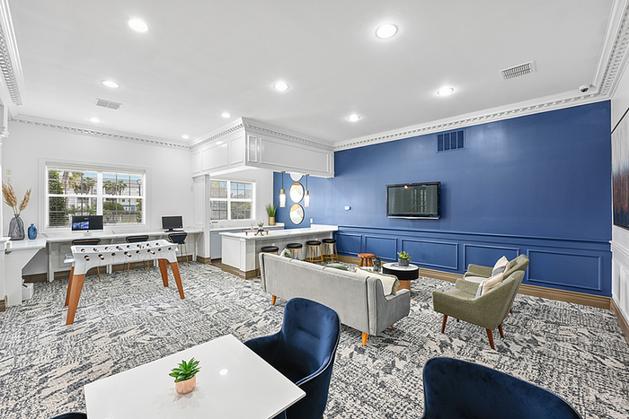 Modern clubhouse space with vibrant blue accent wall, comfortable seating area, and foosball table, ideal for social gatherings and relaxation.