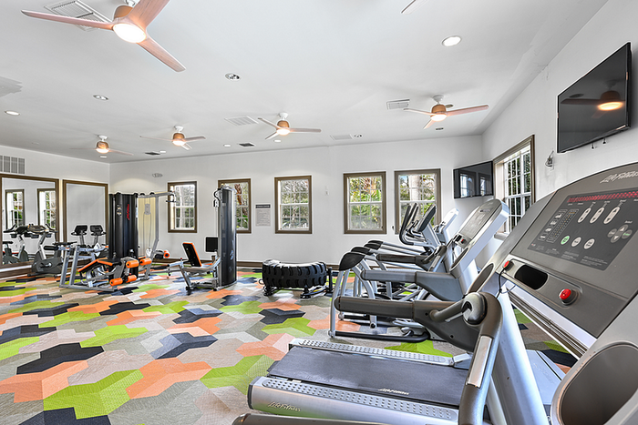 Bright and modern fitness center featuring state-of-the-art cardio machines, weight equipment, and vibrant geometric flooring.