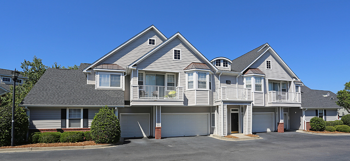 Charming townhouse facade featuring modern architecture with spacious balconies and double garage doors, nestled in a serene suburban setting.