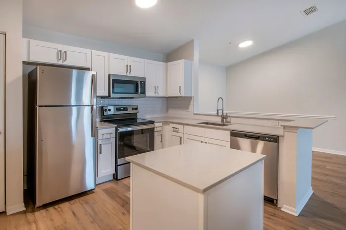 Modern kitchen equipped with stainless steel appliances, large countertops, a floating island, and ample lighting.