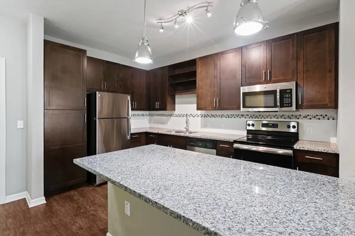Kitchen with granite counters, wood plank floors, espresso custom cabinetry, stainless steel, energy efficient appliances, and tile backsplash at Lantower Asturia.