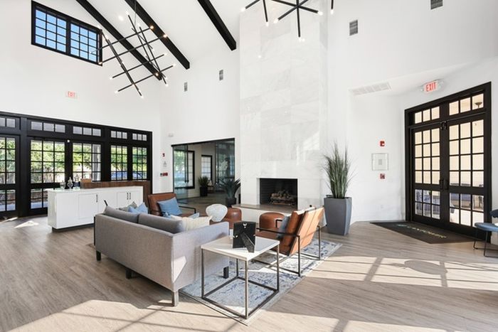 Spacious lounge area in front of the fireplace, with brown chairs, cozy sofas, large window panes for natural lighting, and sound-tech floating plank floors in boardwalk finish at Lantower Round Rock