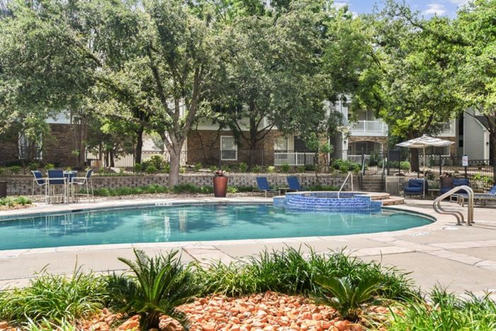 Classic swimming pool area with outdoor seating, pool umbrellas, and a hot tub at Lantower Round Rock.