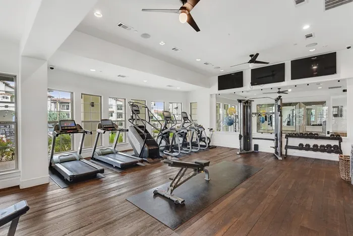 Fully equipped fitness center with free weights, cardio machines, and display monitors at Lantower Ambrosio Apartments.