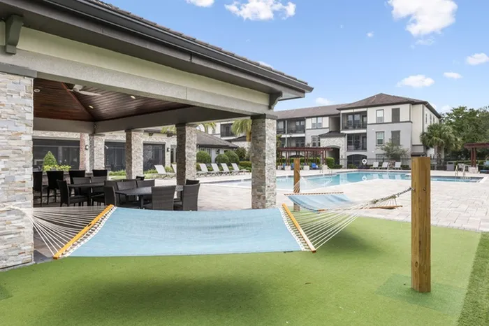An artificial turf area with three hammocks and a resort-style pool in the background at Lantower Grand Pines