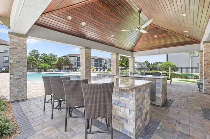A covered veranda with ample seating, a restroom, water fountain, and mini fridge at Lantower Grand Pines with a view of the resort-like pool in the background.