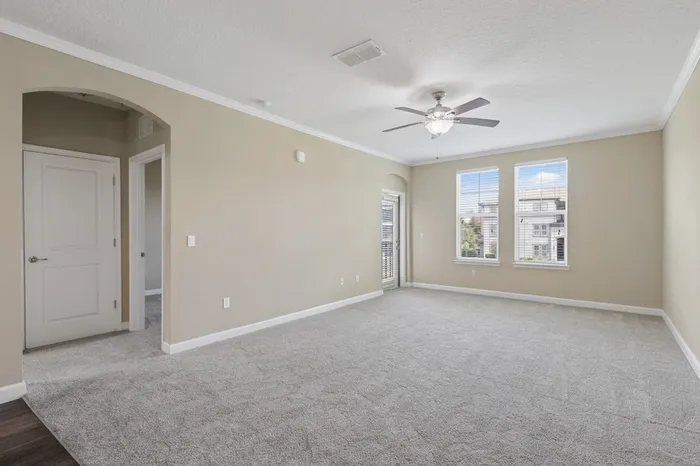 A carpeted, spacious living room with two large windows and a door leading to a balcony at Lantower Grande Pines.