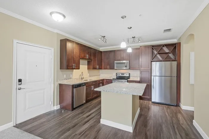 A kitchen with espresso wood cabinetry, wood-style flooring, a kitchen island with a granite countertop, Energy Star Stainless Steel Appliances, and a built-in wine soffit at Lantower Grande Pines.