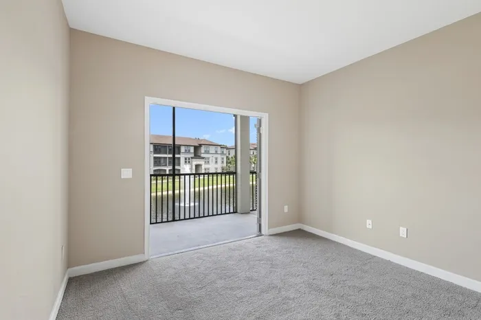 A carpeted room with open French doors leading to the balcony with a view of a pond with a fountain and trees at Lantower Grande Pines.