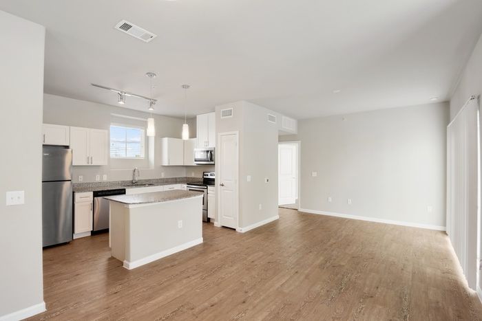 Apartment living room and kitchen with faux wood flooring, granite countertops, and Maytag stainless steel appliances at Lantower Edgewater