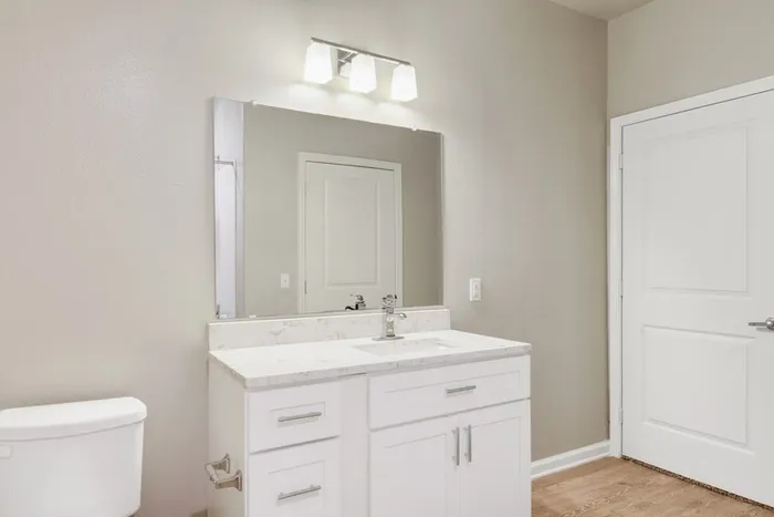 Bathroom with faux wood flooring, granite countertops, with a large square mirror behind a stainless steel sink faucet at Lantower Edgewater
