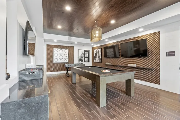 Game room with wall-mounted TVs, a billiard table, and a foosball table at Lantower Grande Flats Apartments.