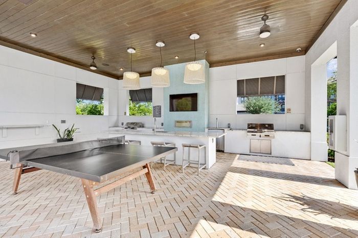 Outdoor kitchen with a ping pong table, kitchen sink, two stainless steel, gas grills, and a wall-mounted TV with a seating area at Lantower Grande Flats Apartments.