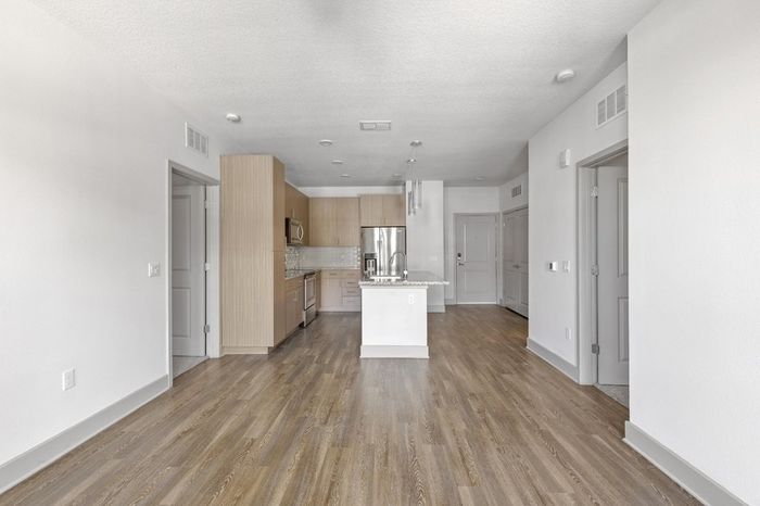 Kitchen with a side-by-side refrigerator, granite countertops, stainless steel appliances, and a kitchen island with the hard-wood floor living room at Lantower Grande Flats.
