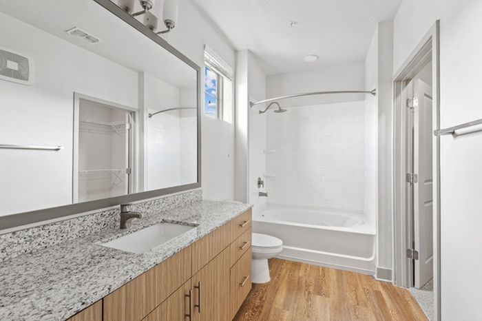 Bathroom with grey, granite countertops and a spacious shower with a high window above the toilet at Lantower Grande Flats.