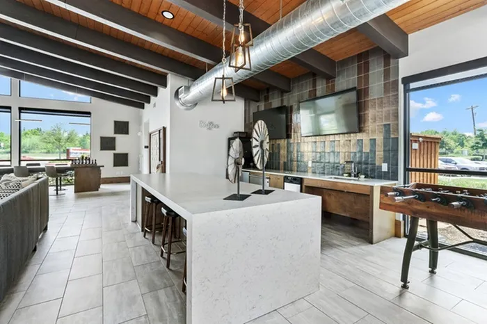 Lounge area with wood-style foosball table, gaming area, stone island equipped with stools, flat screen TVs, and natural lighting at Lantower Legacy Lakes