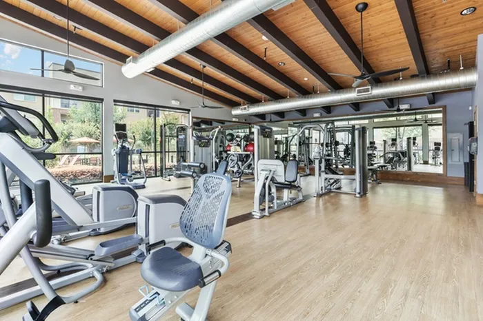 Spacious wood-style flooring with spaced out gym equipment, large mirrors, and windows at Lantower Legacy Lakes
