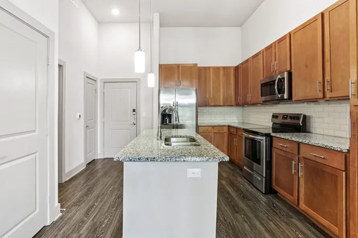 Kitchen with granite countertops, wood-style cabinets, stainless steel appliances, and a kitchen island in the middle at Lantower Legacy Lakes apartments