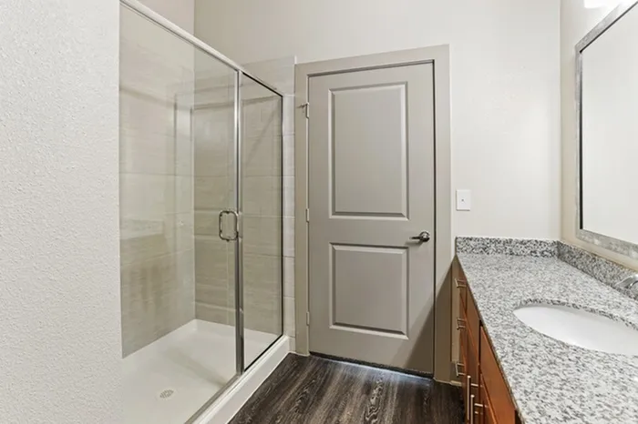 Bathroom with granite countertop and glass sliding door shower with dark stained hardwood flooring at Lantower Legacy Lakes