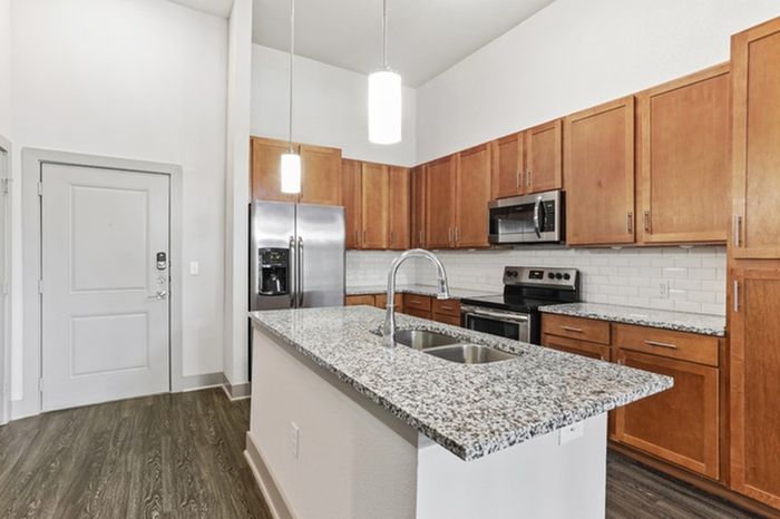 Kitchen with granite countertops, wood-style cabinets, stainless steel appliances, and a kitchen island in the middle at Lantower Legacy Lakes apartments