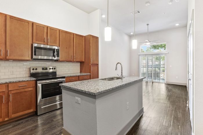 Kitchen with granite countertops, wood-style cabinets, stainless steel appliances, and a kitchen island in the middle at Lantower Legacy Lakes apartments