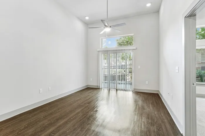 High ceiling room with ceiling fan, dark stained wood-style flooring, with glass sliding door providing natural lighting in Lantower Legacy Lakes' apartment