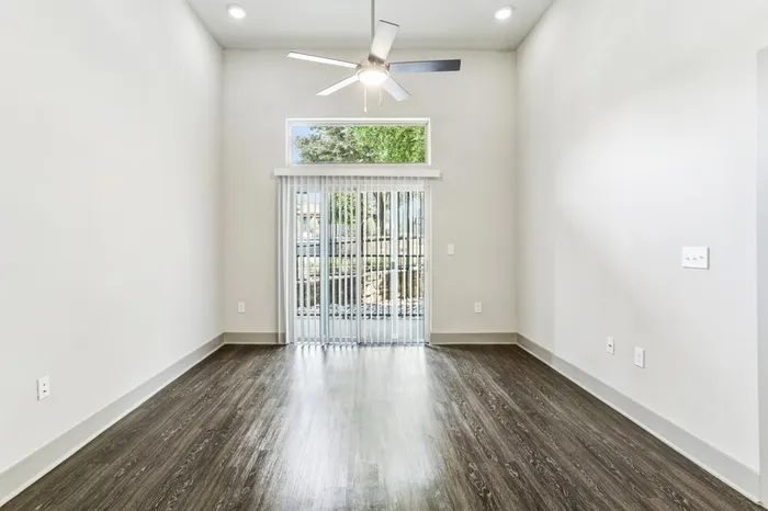 High ceiling room with ceiling fan, dark stained wood-style flooring, with glass sliding door providing natural lighting in Lantower Legacy Lakes' apartment