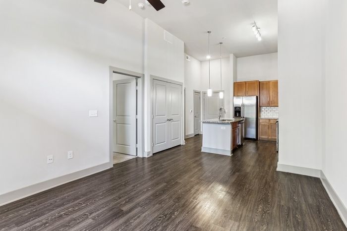 Room and kitchen with granite countertops, wood-style cabinets, stainless steel appliances, and a kitchen island in the middle at Lantower Legacy Lakes apartments
