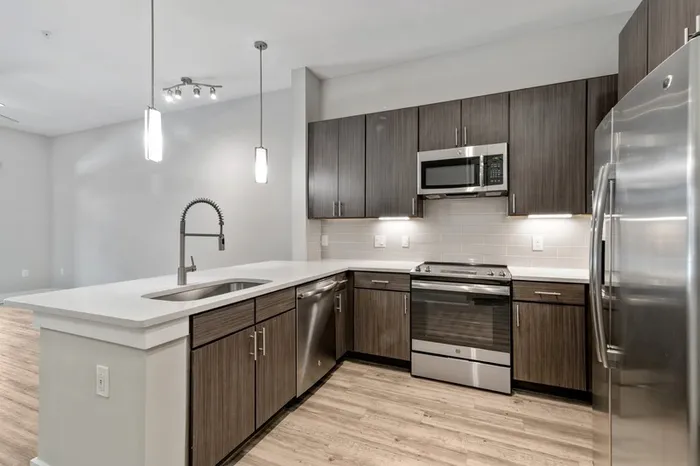 Kitchen with quartz counters, wood-style flooring, dark-colored cabinetry, stainless steel, energy efficient appliances, and tile backsplash at Lantower Weston Corners.