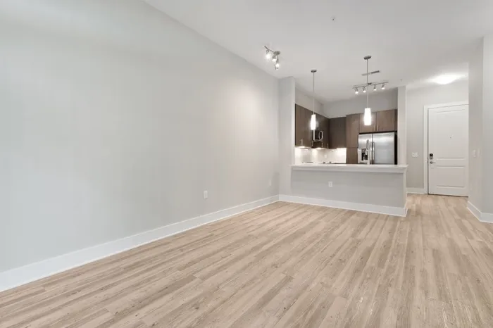 Energy-efficient kitchen with a side-by-side refrigerator, quartz countertops, stainless steel appliances, and a kitchen bar with the wood-style floor living room in the foreground of the image at Lantower Weston Corners.