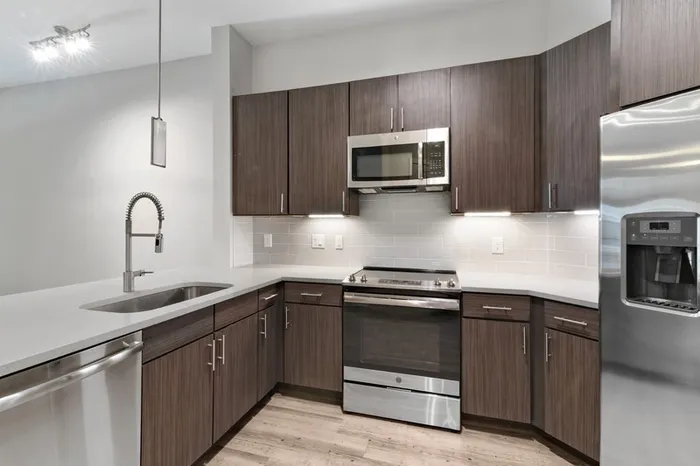 Kitchen with quartz counters, wood-style flooring, dark-colored cabinetry, stainless steel, energy efficient appliances, and tile backsplash at Lantower Weston Corners.