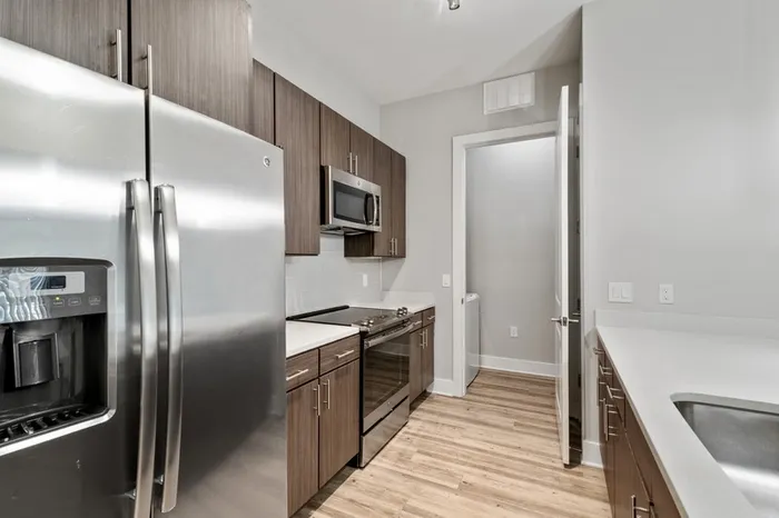 Kitchen with quartz counters, wood-style flooring, dark-colored cabinetry, stainless steel, energy efficient appliances, and tile backsplash at Lantower Weston Corners.