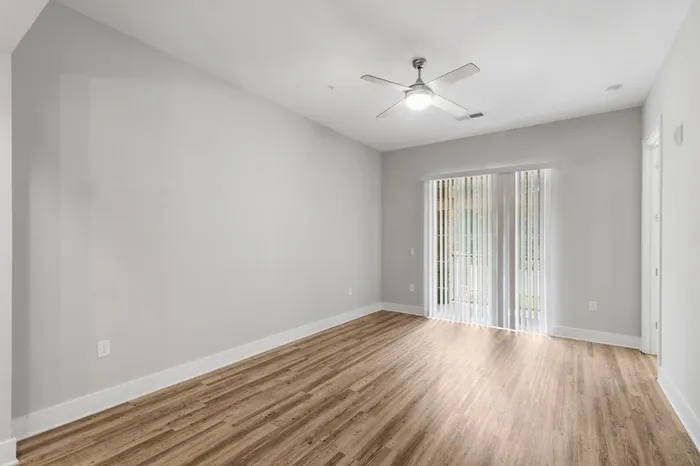 Spacious living room with a ceiling fan, wood-style floors, and a sliding glass door to a balcony at Lantower Weston Corners.