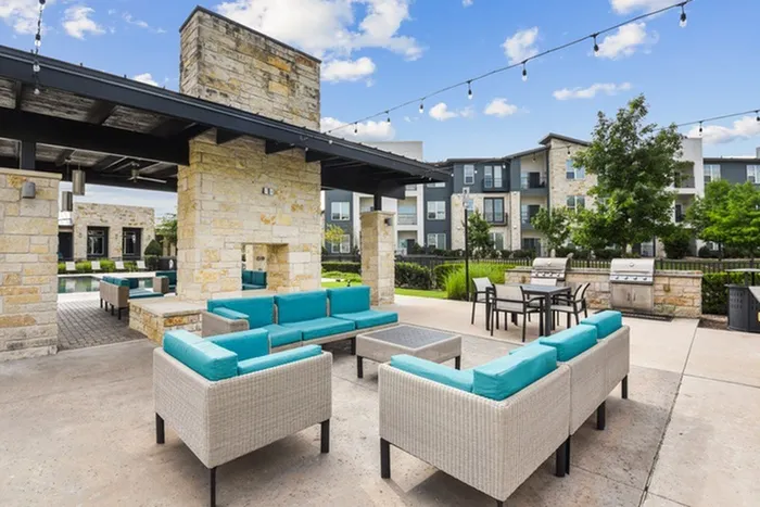 Outdoor poolside lounge area with comfortable sofas and chairs, grills, string lights and a brick fireplace at Lantower Techridge apartments