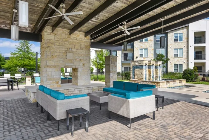 Outdoor poolside lounge area with comfortable sofas and chairs, cooling ceiling fans, a beautiful brick waterfall, string lights and a brick fireplace at Lantower Techridge apartments