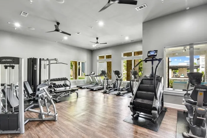 Spacious gym with a variety of gym equipment including free weights and machines, treadmills, stair steppers, and ellipticals all with a pool view at Lantower Techridge apartments