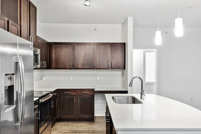 Modern kitchen fit with diamond white quartz countertops and stainless steel sink basin, stainless steel appliances, and an island with overhead lighting at Lantower Techridge apartments