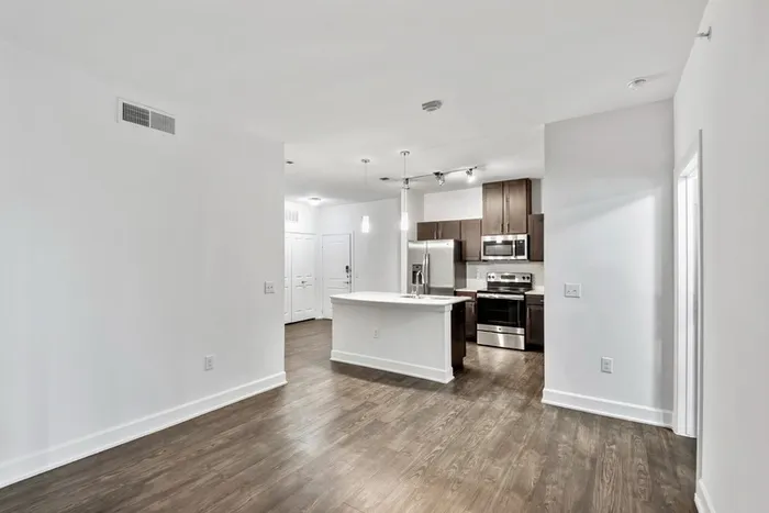 Spacious living and dining room with room for plenty of furniture, connected to Modern kitchen fit with diamond white quartz countertops and stainless steel sink basin, stainless steel appliances, and an island with overhead lighting at Lantower Techridge