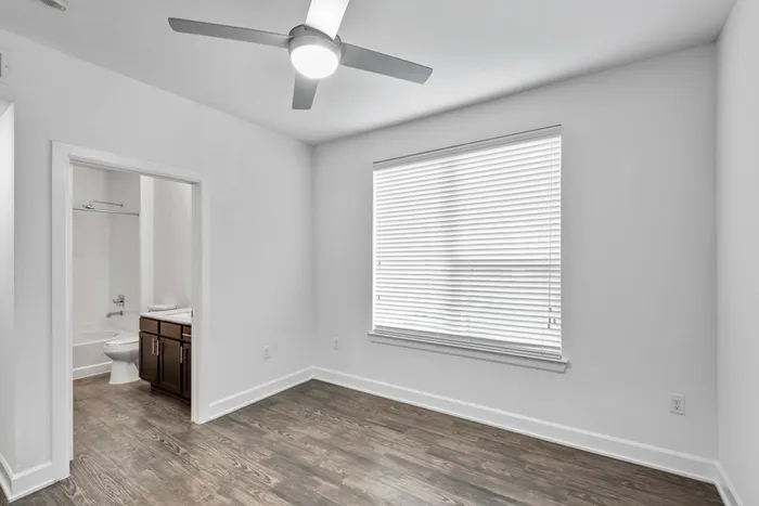 Bedroom and bathroom with vinyl plank flooring, pristine white walls, a large window for beautiful natural lighting and a ceiling fan for cooling in Lantower Techridge apartment