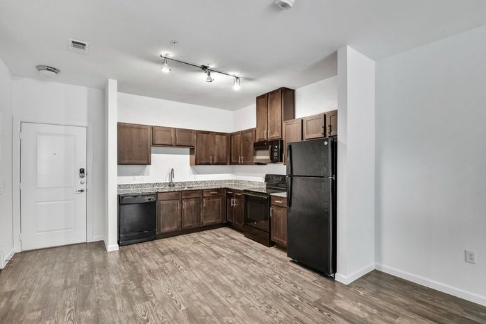 Open and spacious kitchen and living room with dark stained-wood cabinets, black stainless steel appliances, and plenty of room for furniture at Lantower Techridge