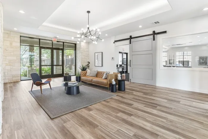 Modern lounging area with a thoughtfully placed artwork, cozy sofas, wood accented chair and architectural chandelier on wood-style plank flooring at Lantower Residences at the Collection